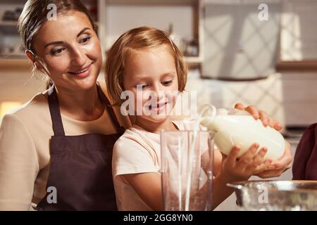 Mère regardant sa fille verser du lait dans la tasse à mesurer Banque D'Images