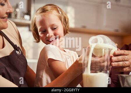 L'enfant rit tout en remplissant le verre de lait avec sa famille Banque D'Images