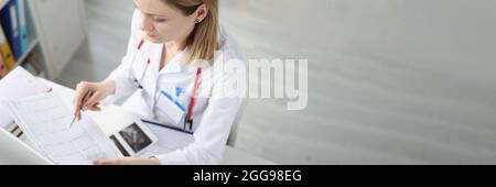 Médecin assis à table et regardant le cardiogramme en clinique Banque D'Images