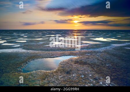 Bel été. La côte de la mer est inclinée par la pierre, le lever du soleil se reflète sur le sable humide. Paysage du matin. Banque D'Images