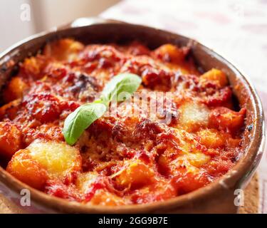 Gnocchi alla Sorrentina, boulettes de pommes de terre italiennes à la sauce tomate, gratinées avec du fromage mozzarella dans un plat en terre cuite. Mise au point sélective. Banque D'Images