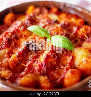 Gnocchi alla Sorrentina, boulettes de pommes de terre italiennes à la sauce tomate, gratinées avec du fromage mozzarella dans un plat en terre cuite. Mise au point sélective. Banque D'Images