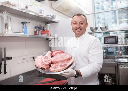 Joyeux chef cuisinier avec des steaks de bœuf marbré, souriant à l'appareil photo Banque D'Images