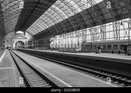 Moscou. Russie. 29 août 2021. Arches voûtées supportant un grand toit en verre recouvrant les rails de la gare et un train s'arrêtant à la plate-forme. Image en noir et blanc. Banque D'Images