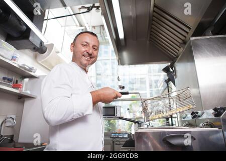 Prise de vue en contre-angle d'un chef homme souriant à l'appareil photo, tout en faisant des frites Banque D'Images