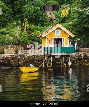 Petite maison jaune colorée et quai avec bateau amarré dans le fjord d'Oslo en Norvège. Le fjord d'Oslo et de minuscules maisons en bois scandinaves classiques Banque D'Images