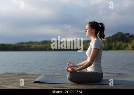 Profil d'une femme détendue faisant de l'exercice de yoga dans un lac au coucher du soleil Banque D'Images