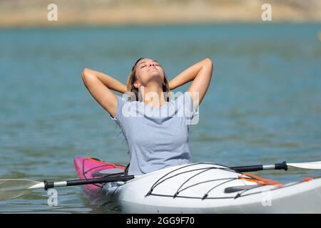 Femme heureuse dans un kayak se relaxant avec les bras sur la tête dans un lac Banque D'Images