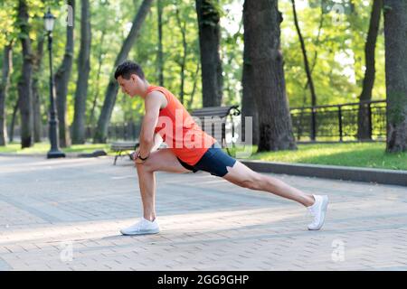 Sportsman tenir la position de fente faire une routine d'étirement pendant l'entraînement sportif en plein air dans le parc, l'échauffement Banque D'Images