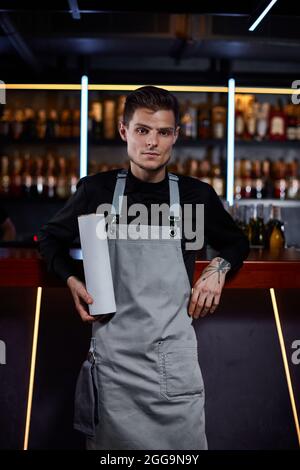 Beau barman en tablier debout au comptoir du bar Banque D'Images