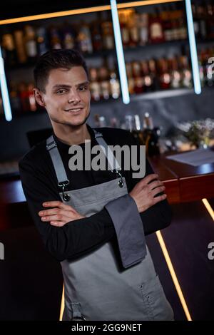 Beau barman en tablier debout au comptoir du bar Banque D'Images