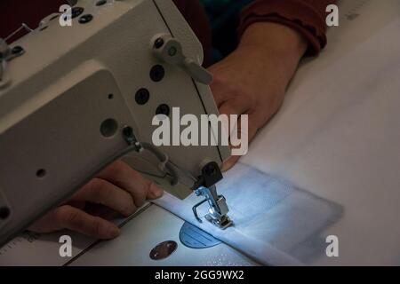 Coudre du tissu avec une machine à coudre. La couture est l'art de fixer ou de fixer des objets à l'aide de points de suture faits avec une aiguille et un fil de couture. Banque D'Images