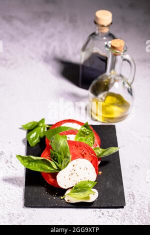 Salade Capresi aux tomates fraîches, mozarella sur une assiette noire avec un pot en verre à l'huile d'olive Banque D'Images