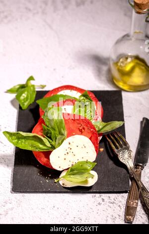 Salade Capresi aux tomates fraîches, mozarella sur une assiette noire avec un pot en verre à l'huile d'olive Banque D'Images