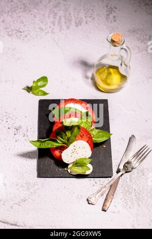 Salade Capresi aux tomates fraîches, mozarella sur une assiette noire avec un pot en verre à l'huile d'olive Banque D'Images