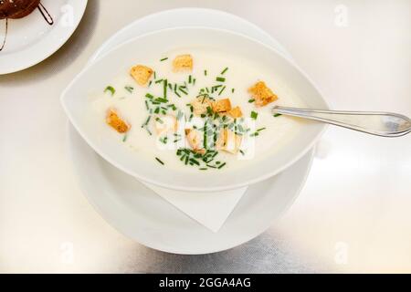 Soupe crémeuse aux croûtons et aux herbes dans une assiette blanche sur une table dans un restaurant. Gastro tourisme après la quarantaine. Soupe à la crème d'oignon sur une table wi Banque D'Images