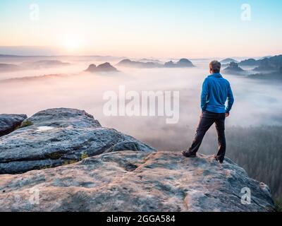 Randonneur solitaire se relaxant sur la montagne et regardant le coucher de soleil sur la vallée brumeuse Banque D'Images