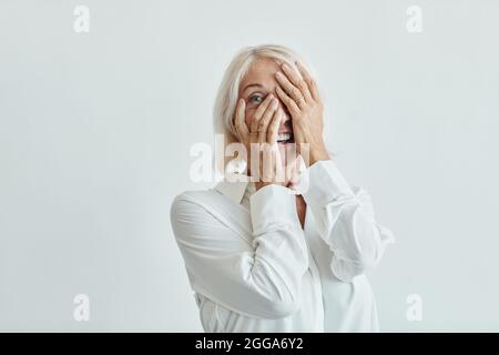 Portrait de la taille vers le haut d'une femme mûre élégante riant sans souci sur fond blanc, espace de copie Banque D'Images