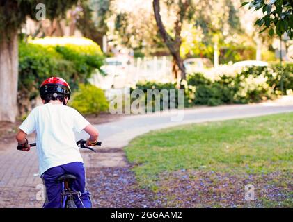 Jeune garçon porte un casque tout en montant son vélo dans le parc Banque D'Images