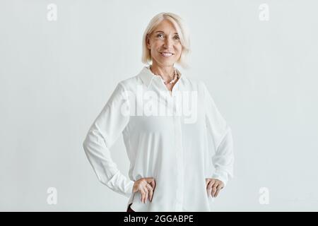 Portrait à la taille haute d'une femme élégante et mûre souriant à l'appareil photo tout en posant en toute confiance sur fond blanc, espace de copie Banque D'Images