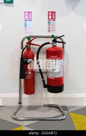 Une paire d'extincteurs rouges - eau et dioxyde de carbone - sur un rack de support dans un bureau avec des notices / panneaux de sécurité, Royaume-Uni Banque D'Images