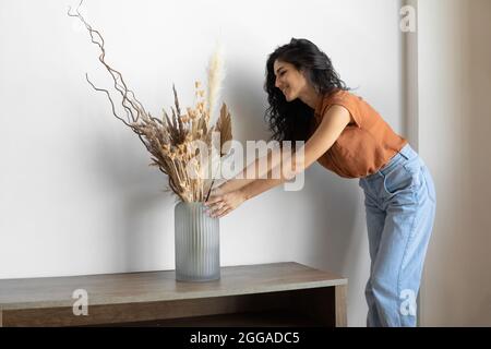 Décoration intérieure moderne et minimaliste. Jeune femme organisant des plantes séchées dans un vase, créant une atmosphère chaleureuse dans la maison Banque D'Images