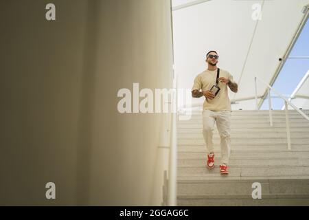 Jeune homme de style caucasien avec tatouages et lunettes de soleil debout sur l'escalier Banque D'Images