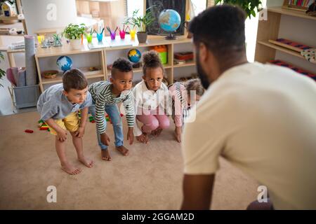 Groupe de petits enfants de la maternelle avec homme enseignant à l'intérieur dans la salle de classe, faisant de l'exercice. Banque D'Images