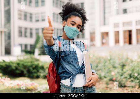 Black Student Girl in face Mask gestante Thumbs-Up posant à l'extérieur Banque D'Images