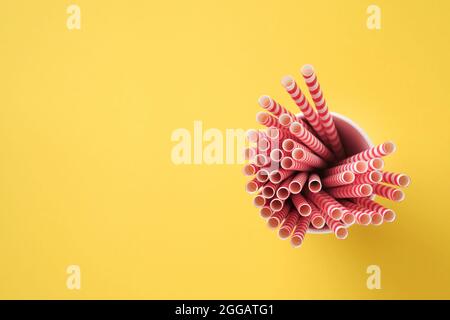 Tubes à boire rouge et marron en papier et fécule de maïs, matériau biodégradable et verres en papier écologique sur fond jaune et gris tendance couleur 2021 Banque D'Images