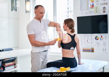 Jeune femme assise sur massage pendant que le médecin ostéopathe application de ruban jaune dans le bureau médical Banque D'Images