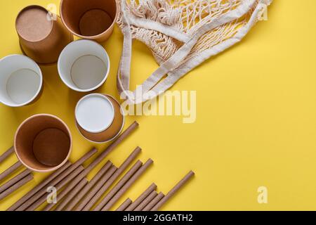 Tubes bruns à boire pailles en papier et fécule de maïs, sac de filet et tasses de café en papier vides sur fond gris et jaune tendance. Zéro était Banque D'Images