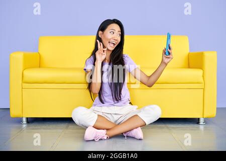 Une femme asiatique souriante vlogger enregistrant une vidéo sur un téléphone portable montrant le signe de la victoire. Technologie, concept de communication Banque D'Images