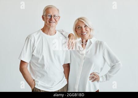 Portrait minimal de couple senior moderne, vêtu de blanc sur fond blanc et souriant à l'appareil photo Banque D'Images