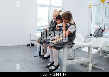 Sympa, les petites filles s'asseyant sur le bureau, s'amusent. Vue porte ouverte. Dans une salle de classe lumineuse. Banque D'Images