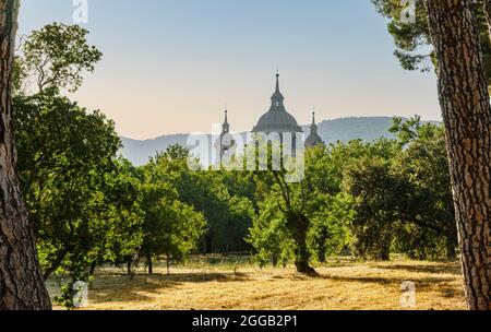 Vue au coucher du soleil sur le dôme et les tours du monastère San Lorenzo de l'Escorial depuis une forêt au début de l'automne et les montagnes en arrière-plan. Banque D'Images
