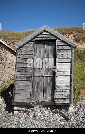 Hangar en bois patiné sur une plage de galets à l'île Sainte, Northumberland, Angleterre. Banque D'Images