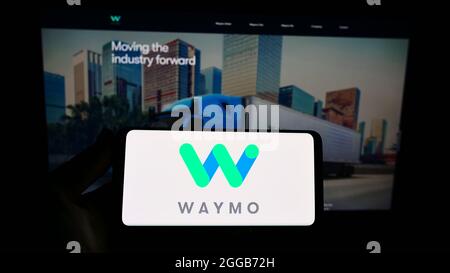 Personne tenant un téléphone portable avec le logo de la compagnie américaine autonome de conduite Waymo LLC sur l'écran en face de la page Web d'affaires. Mise au point sur l'affichage du téléphone. Banque D'Images