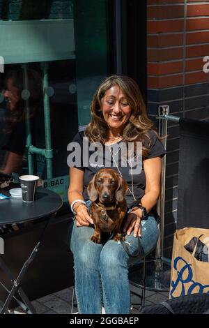 Bracknell, Berkshire, Royaume-Uni. 28 août 2021. Une dame s'assoit avec son chien de saucisse dans le centre-ville de Bracknell. Crédit : Maureen McLean/Alay Banque D'Images