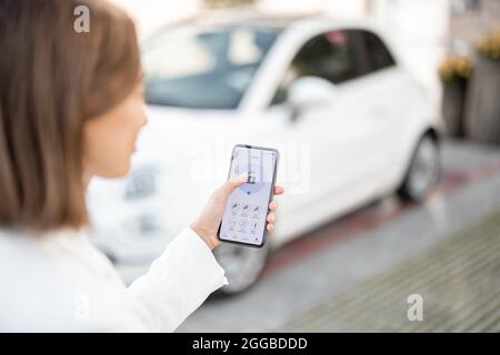 Une femme contrôle l'alarme de voiture avec un téléphone portable Banque D'Images