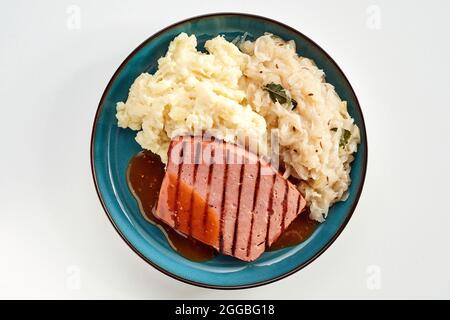 Service de spécialité de pain de viande cuit allemand bruni sur un grill avec purée de pommes de terre et de chou sur une assiette en faïence bleue dans une vue sur blanc couché Banque D'Images