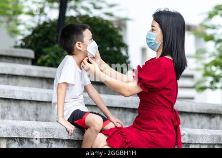 Maman porte un masque médical pour son enfant. Petit garçon asiatique et maman dans le masque médical. Concept asiatique de virus de protection de la famille. Banque D'Images