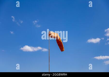 Bonnette anti-vent pointant vers la position du vent. Windsock en orange avec ciel bleu en arrière-plan, également connu sous le nom de 'Biruta de Vento' en portugais. Banque D'Images