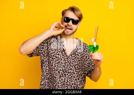 Photo de funky cool jeune gentleman habillé imprimer chemise verres foncés fumer boire cocktail isolé couleur jaune fond Banque D'Images