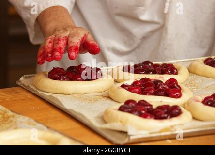 La femme sur la photo fait des tartes aux fruits. Les mains remplissent la pâte à tarte avec des fraises. Travail dans la boulangerie. Banque D'Images