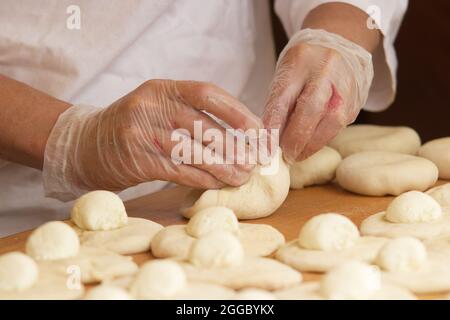 La femme sur la photo fait des tartes farcies. Les mains en gants de protection enveloppent la garniture de la pâte à levure. Travail dans la boulangerie. Banque D'Images