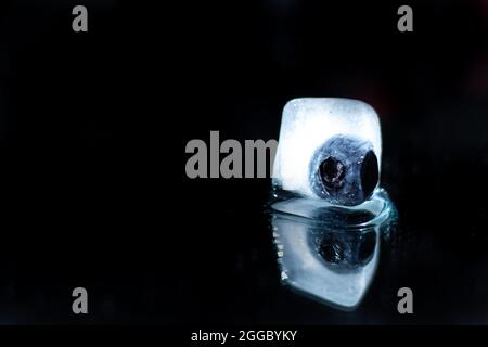 Gros plan de myrtille congelée dans un cube de glace isolé sur fond noir; photographie créative des aliments; arôme d'eau Banque D'Images