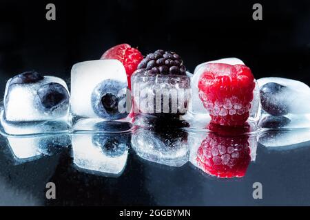 Gros plan des bleuets, framboises et mûres congelées dans des glaçons isolés sur fond noir avec espace de copie; arôme d'eau sain Banque D'Images