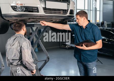 Un mécanicien s'adresse à un directeur dans le cadre d'un service de véhicule en voiture. Bossage montrant ce qu'il faut corriger Banque D'Images