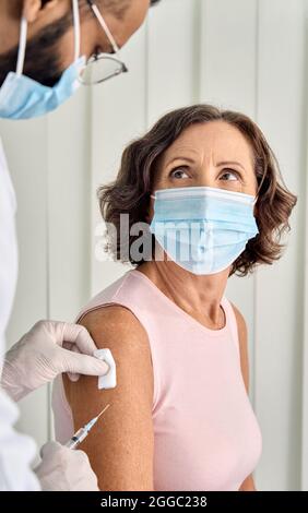 Une femme plus âgée, portant un masque facial, reçoit une injection de vaccination en clinique. Verticale. Banque D'Images